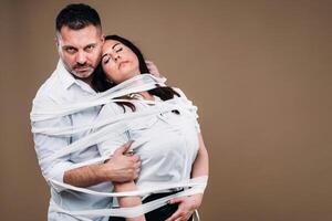 An aggressive man embraces a battered woman and is wrapped in bandages together. Domestic violence photo