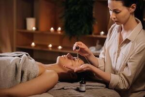 A female cosmetologist holds a pipette with essential oil before aromatherapy and massage to the patient. aromatherapy photo