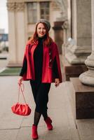 A beautiful stylish woman dressed in an elegant red coat with a stylish red handbag in the autumn city photo