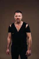 Against a gray background stands a battered angry man in a black T-shirt with wounds photo