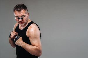 on a gray background stands a battered man in a black T shirt looking like a fighter and preparing for a fight photo