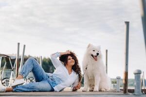 a happy woman with a big white dog lies on a pier near the sea at sunset photo