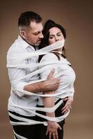An aggressive man embraces a battered woman and is wrapped in bandages together. Domestic violence photo