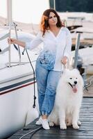 a happy woman with a big white dog stands on the pier near the yacht photo