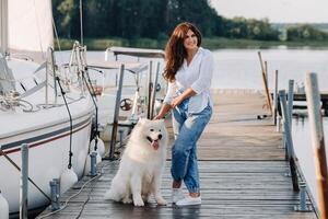 a happy woman with a big white dog stands on the pier near the yacht photo