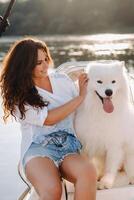 un contento mujer con un grande blanco perro en un blanco yate en el mar foto