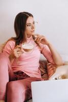 a girl in the morning in pajamas at home working on a laptop with drinking coffee, a girl self-isolated at home and resting on the couch and watching a laptop.Household chores photo