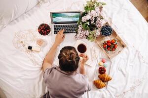 a girl sits in bed in the evening, with a smartphone in her hand and eats strawberries, a girl in bed has sweets before going to bed. photo