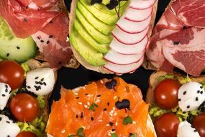 Assorted sandwiches with fish, cheese, meat and vegetables on a black plate photo