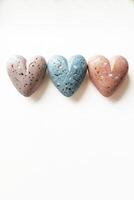 AI generated Three terrazzo style heart shaped stones in pastel colors aligned on a white background, symbolizing love and tenderness, suitable for Valentines Day promotions or romantic concepts photo