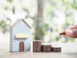 Close up of hand putting coins into stack of coins and Miniature house. The concept of saving money for house, Property investment, House mortgage, Real estate photo