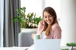 joven negocio mujer en el oficina Bebiendo café y mirando mediante un ventana foto