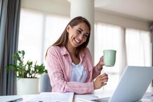 joven negocio mujer en el oficina Bebiendo café y mirando mediante un ventana foto