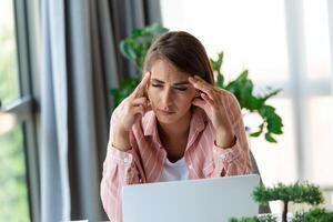 Exhausted businesswoman having a headache in modern office. Creative woman working at office desk feeling tired. Stressed casual business woman feeling head pain while overworking on desktop computer. photo