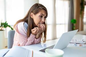 Young woman biting her nails while working on a laptop at home. Anxious woman working in office biting her fingers and nails. photo