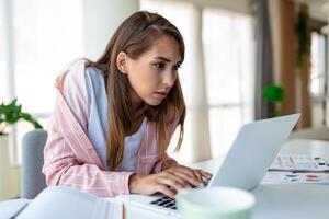 joven mujer trabajando ordenador portátil. negocio mujer ocupado trabajando en ordenador portátil computadora a oficina. mujer de negocios sentado a brillante moderno trabajo estación y mecanografía en ordenador portátil foto