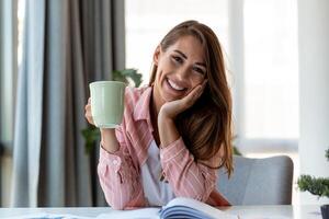 joven negocio mujer en el oficina Bebiendo café y mirando a el cámara foto