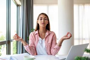 calma mujer relajante meditando con computadora portátil, No estrés gratis alivio a trabajo concepto, consciente de pacífico joven mujer de negocios o estudiante practicando respiración yoga ejercicios a lugar de trabajo, oficina meditación foto