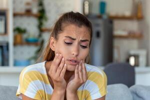 Portrait of unhappy young woman suffering from toothache at home. Healthcare, dental health and problem concept. photo