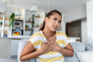 Stressed young woman feeling pain and touching chest suffer from heartache disease at home while having heart attack, infarction photo