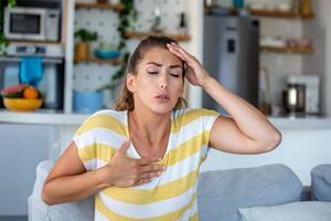 Stressed young woman feeling pain and touching chest suffer from heartache disease at home while having heart attack, infarction photo