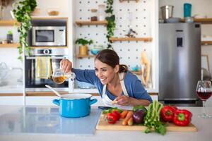 contento joven mujer Cocinando saboreo cena en un maceta en pie en moderno cocina a hogar. ama de casa preparando sano comida sonriente . casa y nutrición. dieta recetas concepto foto