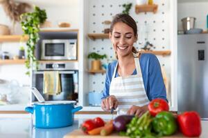 hermosa joven mujer estar a moderno cocina picar vegetales preparar Fresco vegetal ensalada para cena o almuerzo, joven mujer Cocinando a hogar hacer desayuno seguir sano dieta, vegetariano concepto foto