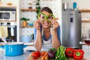 Photo of young woman smiling while cooking salad with fresh vegetables in kitchen interior at home