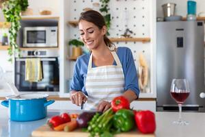 hermosa joven mujer estar a moderno cocina picar vegetales preparar Fresco vegetal ensalada para cena o almuerzo, joven mujer Cocinando a hogar hacer desayuno seguir sano dieta, vegetariano concepto foto