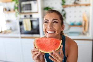 Young woman eats a slice of watermelon in the kitchen. Portrait of young woman enjoying a watermelon. photo