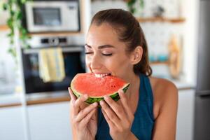 Young woman eats a slice of watermelon in the kitchen. Portrait of young woman enjoying a watermelon. photo