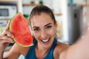 Young woman eats a slice of watermelon in the kitchen. Portrait of young woman enjoying a watermelon. photo