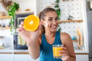 hermosa joven mujer Bebiendo Fresco naranja jugo en cocina. sano dieta. contento joven mujer con vaso de jugo y naranja a mesa en cocina. foto