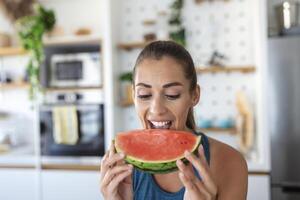 joven mujer come un rebanada de sandía en el cocina. retrato de joven mujer disfrutando un sandía. foto