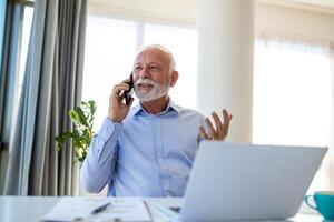 Mature businessman working on laptop and talking on cellphone. Handsome mature business leader sitting in a modern office photo