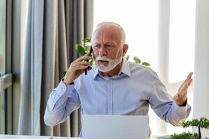 Mature businessman working on laptop and talking on cellphone. Handsome mature business leader sitting in a modern office photo