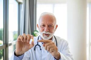 Doctor online. Senior medic talking to client on laptop computer from his office. Mature male therapist explaining medical treatment to patient through a video call with laptop in the consultation. photo