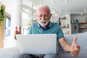 mayor hombre sentado en sofá mirando a ordenador portátil pantalla gritar con alegría siente emocionado contento celebrando lotería victoria, suerte momento, tiene en línea oportunidad, ventas y descuentos comercio electrónico concepto foto