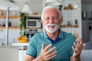 Smiling senior man wave to camera having video call on laptop, happy elderly male sit on couch at home talk using modern technologies and wireless connection photo