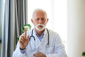 Doctor online. Senior medic talking to client on laptop computer from his office. Mature male therapist explaining medical treatment to patient through a video call with laptop in the consultation. photo