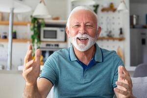 Smiling senior man wave to camera having video call on laptop, happy elderly male sit on couch at home talk using modern technologies and wireless connection photo