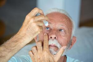 hombre poniendo líquido gotas en su ojo resolviendo visión problema.senior goteante ojo soltar medicina curación su ojo dolor. visión y oftalmología medicamento, mayor gris pelo hombre aplicando ojo gota. foto