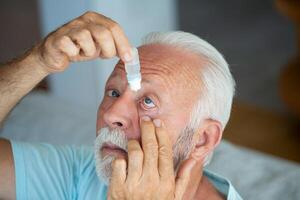 hombre poniendo líquido gotas en su ojo resolviendo visión problema.senior goteante ojo soltar medicina curación su ojo dolor. visión y oftalmología medicamento, mayor gris pelo hombre aplicando ojo gota. foto