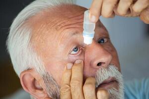 Man putting liquid drops in his eye solving vision problem.Senior dropping eye drop medicine healing his eye pain. Vision and ophthalmology medicine, Senior gray hair man applying eye drop. photo