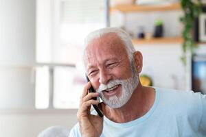 Senior man talking on mobile phone at home. Laughing senior man talking on a cellphone while relaxing in a chair in his living room photo