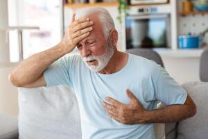 Senior man presses hand to chest has heart attack suffers from unbearable pain, Mature man with pain on heart in living room. Senior man suffering from bad pain in his chest heart attack at home photo
