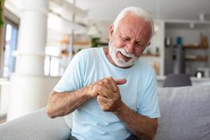 mayor hombre tiene dolor en dedos y manos. antiguo hombre con dedo dolor, hombre masajear su artrítico mano y muñeca. foto