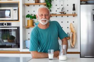 mayor hombre Bebiendo un vaso de Leche con un contento cara en pie y sonriente. hermoso mayor hombre Bebiendo un vaso de Fresco Leche en el cocina foto