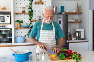 contento retirado mayor hombre Cocinando en cocina. Jubilación, pasatiempo personas concepto. retrato de sonriente mayor hombre corte vegetales foto