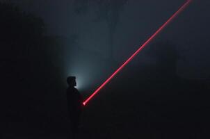 long exposure shot of silhouette of man holding a red laser photo